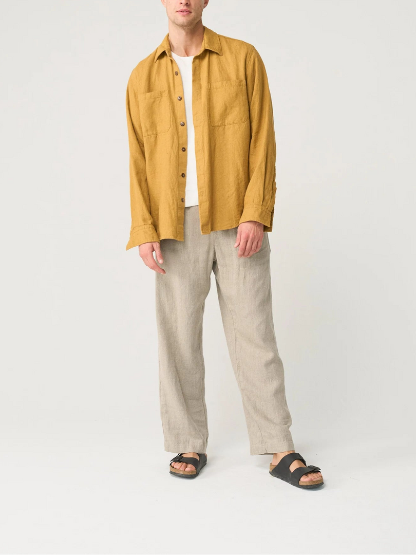 Man wearing a mustard yellow shirt and beige pants on a white background